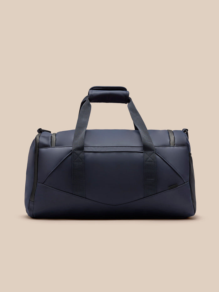 Midnight blue Castore holdall shown from the front with dual top handles and a front logo badge.