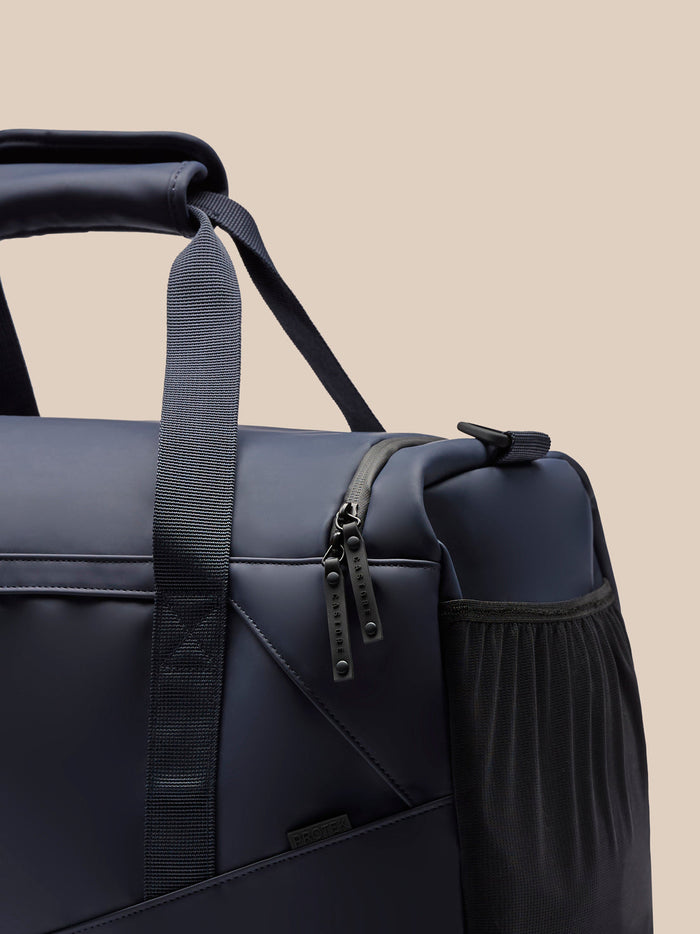 Close up of Core Holdall in midnight blue showing padded grab handle, strap and front zipper pulls.