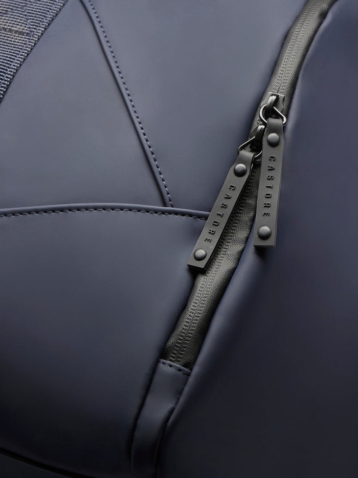 Detail of Core Holdall zipper with branded pulls on navy polyurethane exterior.