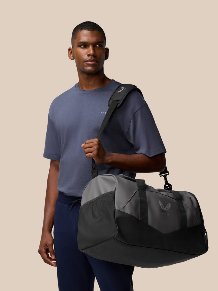 Male model wearing a Core Holdall over the shoulder showcasing a compact travel bag in gunmetal black