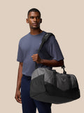 Male model wearing a Core Holdall over the shoulder showcasing a compact travel bag in gunmetal black