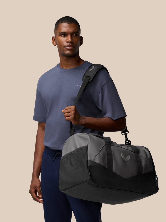 Male model wearing a Core Holdall over the shoulder showcasing a compact travel bag in gunmetal black