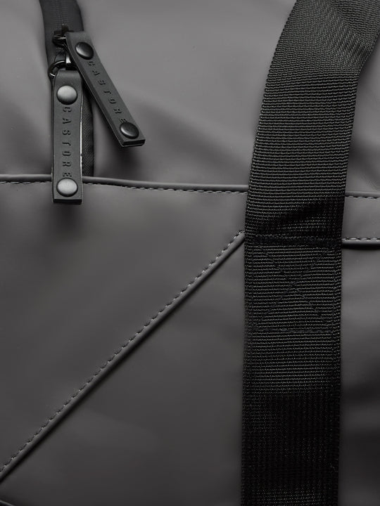 Close-up of gunmetal Core Holdall zipper and strap on dark PU exterior.