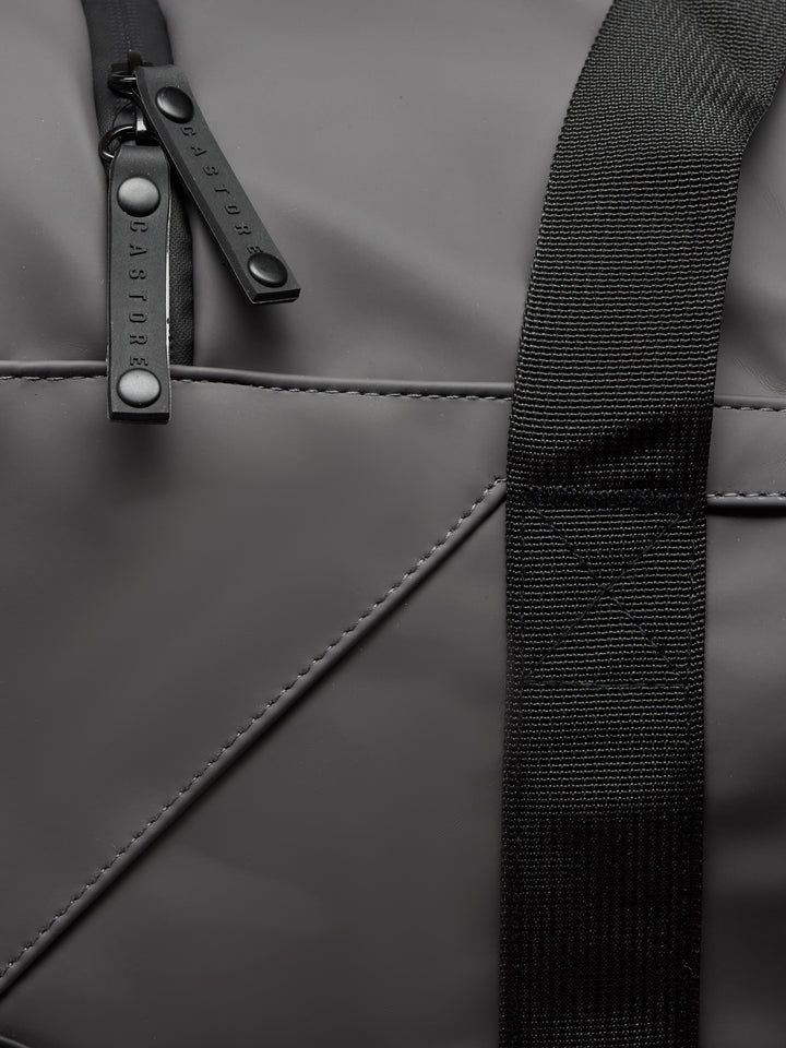 Close-up of gunmetal Core Holdall zipper and strap on dark PU exterior.
