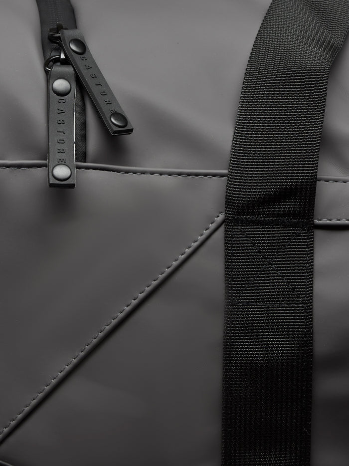 Close-up of gunmetal Core Holdall zipper and strap on dark PU exterior.
