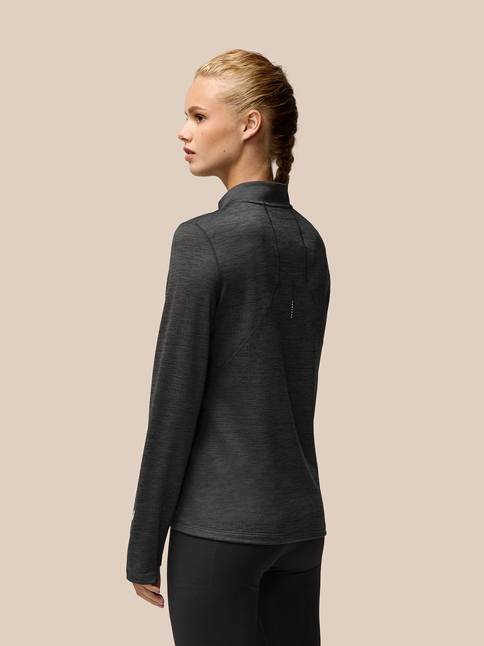 Back view of a woman wearing a dark gray Flow Training 1/2 Zip Top showing seam panels and left sleeve logo