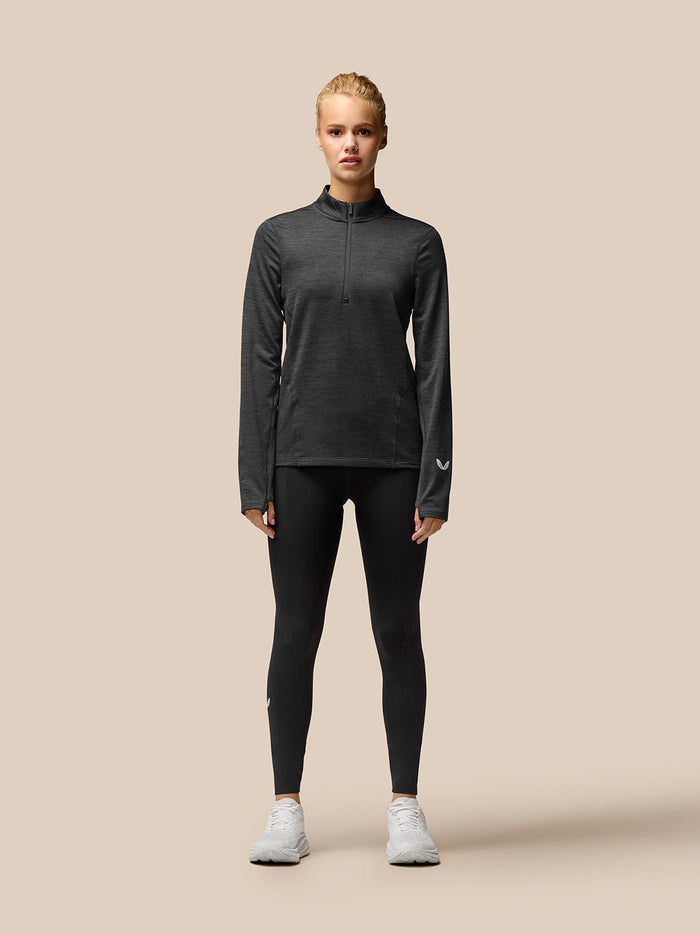 Woman wearing Flow Training 1/2 Zip Top in black, full body view showing funnel collar half zip and thumbholes.
