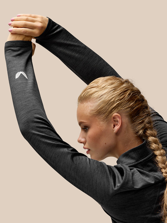 Model in Flow Training Top with long sleeves, arms raised, logo visible on the left sleeve.