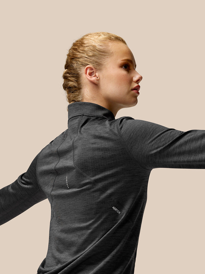 Side profile of a woman wearing a Flow Training half zip top in black charcoal with a funnel collar and seam details