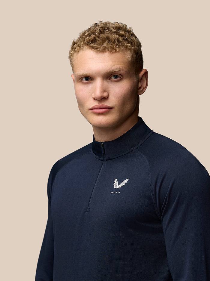 Front view of navy Adapt Training top with Castore logo on left chest and a high collar zip