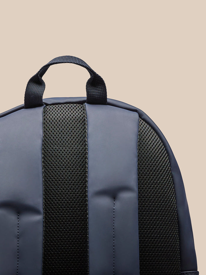 Close up of the Active Backpack Navy top handle and strap against a beige background.