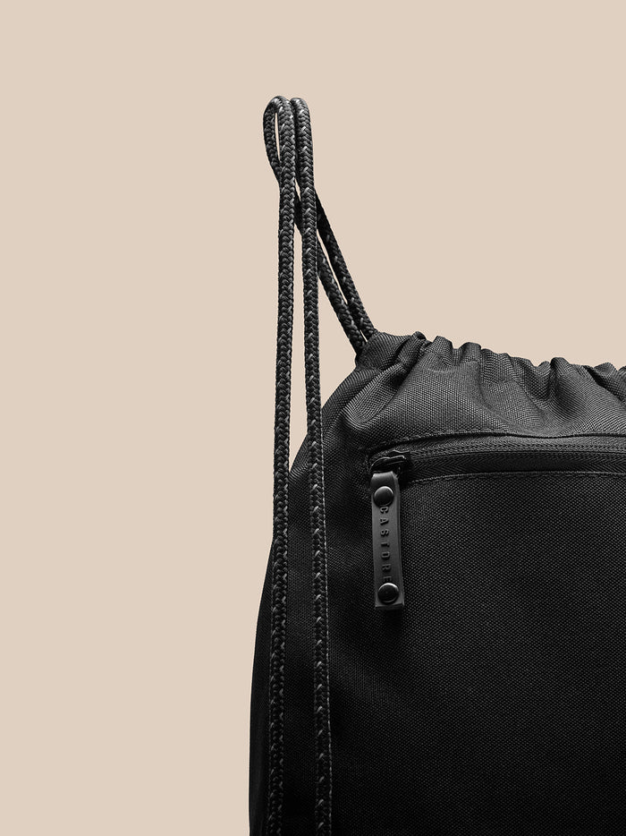 Close up of a black Castore gym bag with braided drawstrings and a zipper pull