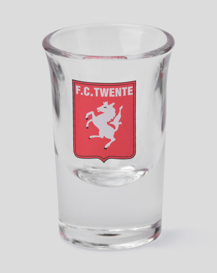 Close up of an FC Twente shot glass with red crest on clear glass.
