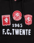 Close up of black hoodie chest displaying three FC Twente patches left and right shield emblems and central circular crest