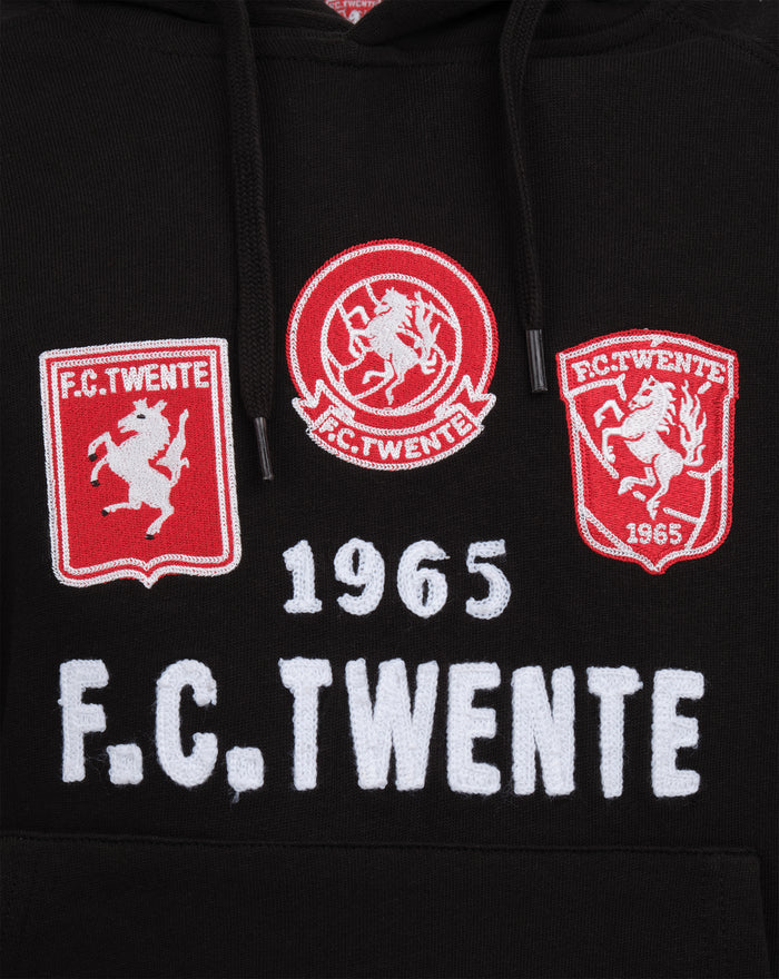 Close up of black hoodie chest displaying three FC Twente patches left and right shield emblems and central circular crest