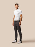 Full-body shot of a man in a white golf polo with Castore logo on the chest, paired with gray trousers.