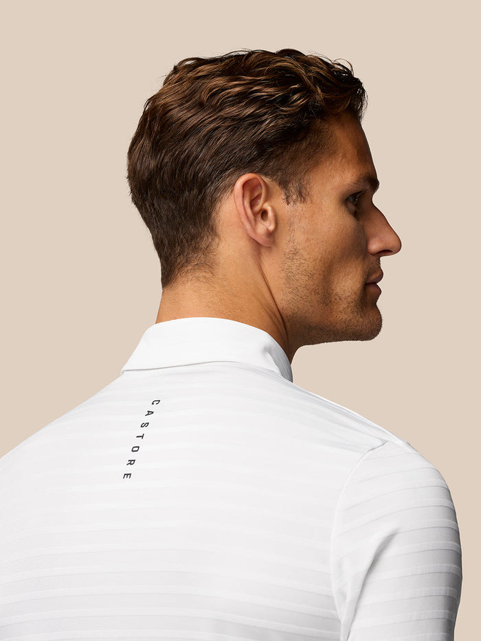 Three-quarter back view of a man in a white textured polo with Castore branding along the upper back.