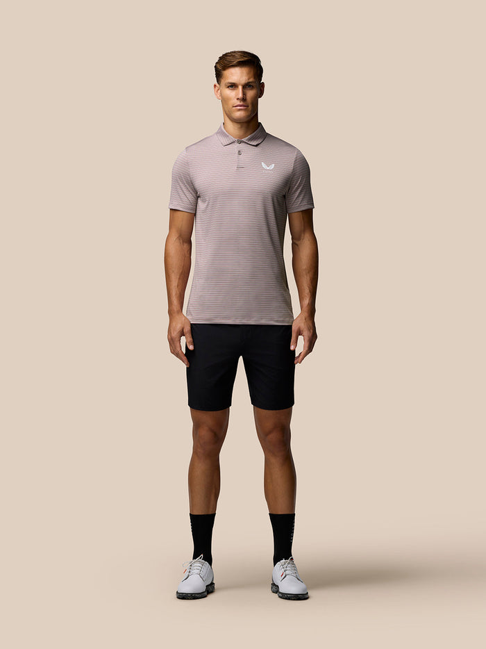 Full-body shot of a male model wearing a pink striped golf polo with Castore logo on the chest and black shorts