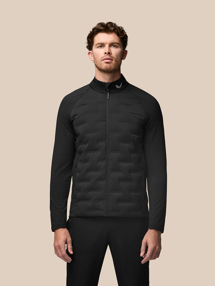 Full body shot of a man in a black stand up collar quilted golf jacket, zipped up, against a beige background