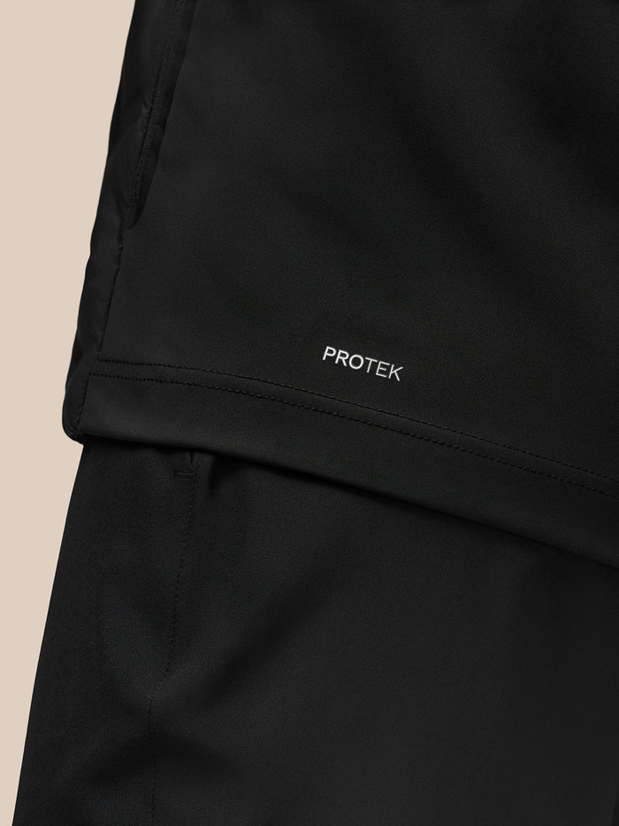 Lower back close-up of the black jacket showing PROTEK branding on the hem.