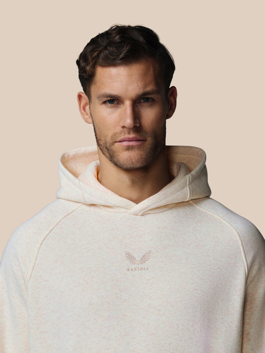 Close-up van model met oatmeal marl hoodie, geborduurd Castore-logo op borst zichtbaar