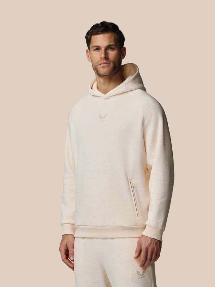 Male model wearing oatmeal cotton fleece hoodie with Castore logo on chest and zip pocket