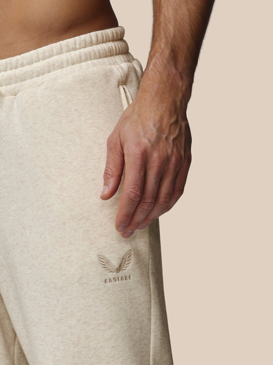 Close-up view of beige fleece joggers with an elastic waistband and embroidered Castore logo on the left thigh.