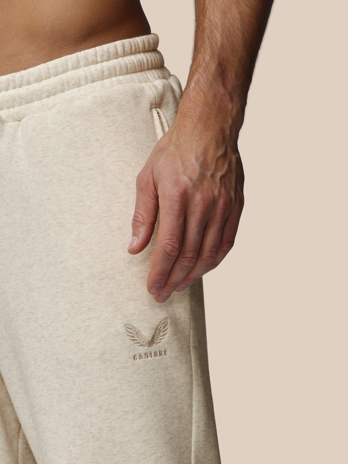 Close-up view of beige fleece joggers with an elastic waistband and embroidered Castore logo on the left thigh.