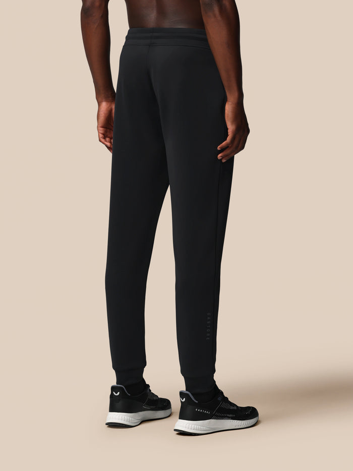 Back view of a male model wearing black Flex Joggers with an elastic waistband and logo on the left thigh