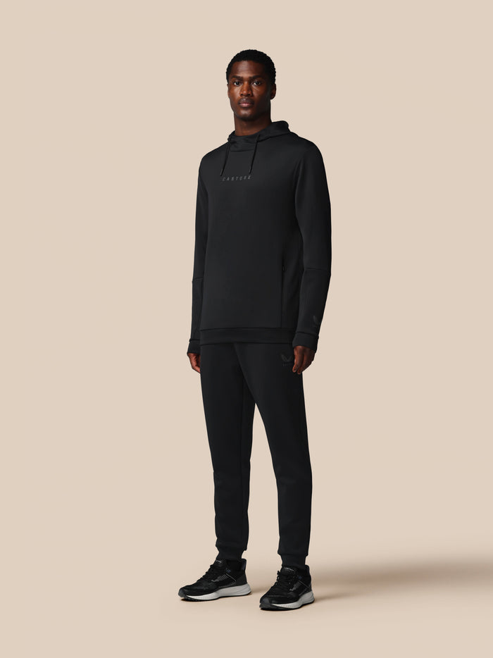 Front view of a male model in a black Castore hoodie and matching joggers with logos on chest and leg