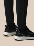 Lower leg view of black Heren Flex Joggers with vertical Castore logo next to athletic shoes