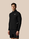 Man draagt zwarte Apex Training Gilet zonder mouwen met Castore logo op linkerborst tegen een beige achtergrond