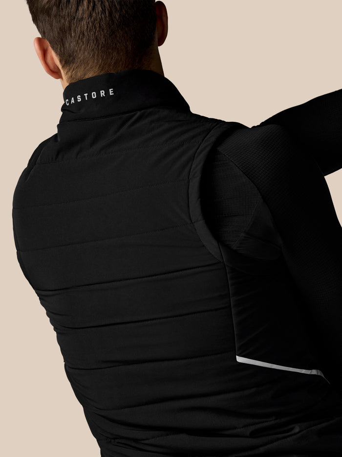 Back collar of a black Apex Gilet with white Castore text against a beige background