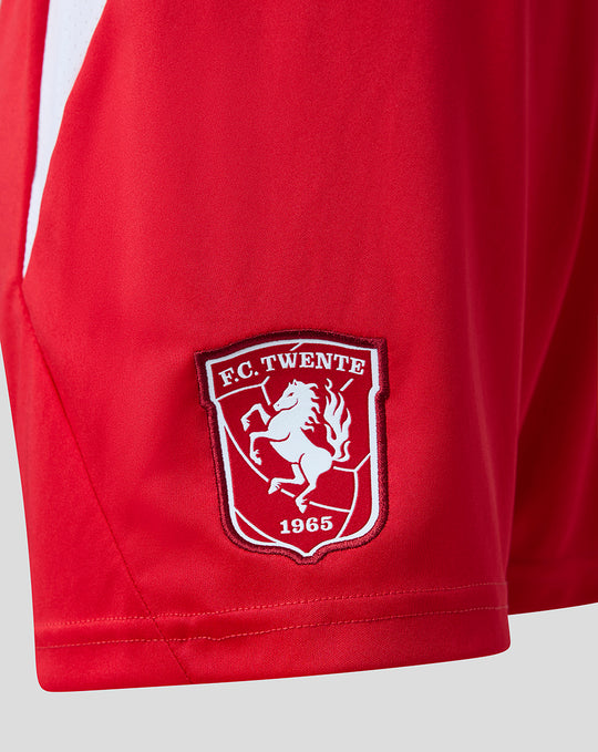 Close-up of FC Twente badge on red junior home shorts.