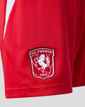 Close-up of FC Twente badge on red junior home shorts.