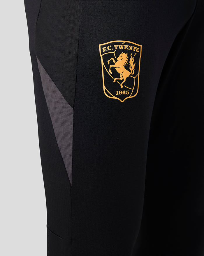 Close-up of left thigh showing gold FC Twente crest on black training pants.