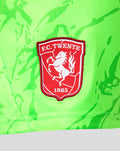Close-up of red FC Twente crest badge on neon green keeper shorts.
