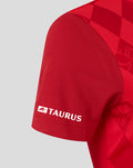 Close-up of the red shirt sleeve showing Taurus branding on the cuff with textured knit and diamond pattern continuing.