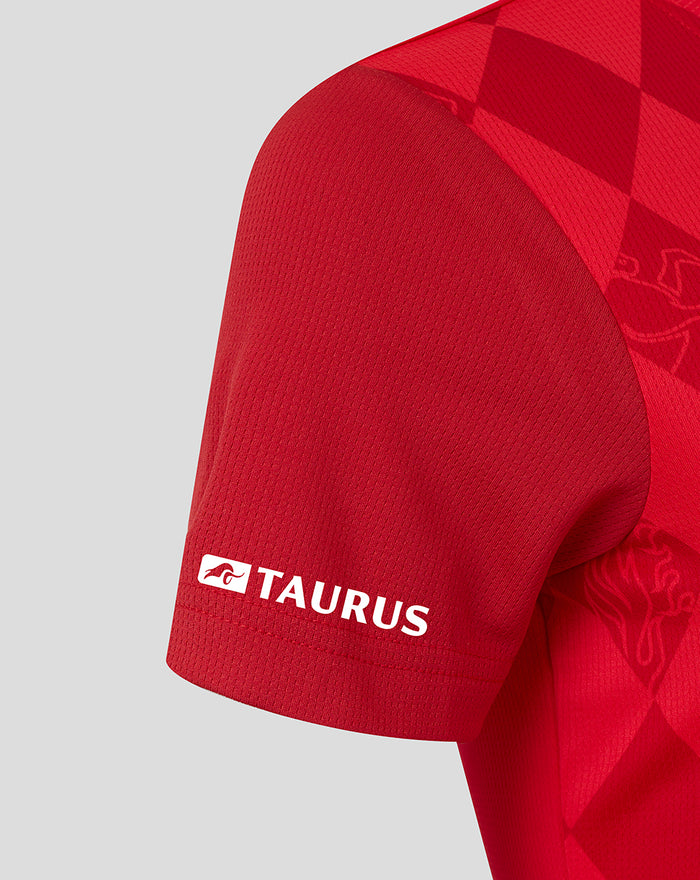 Close-up of the red shirt sleeve showing Taurus branding on the cuff with textured knit and diamond pattern continuing.
