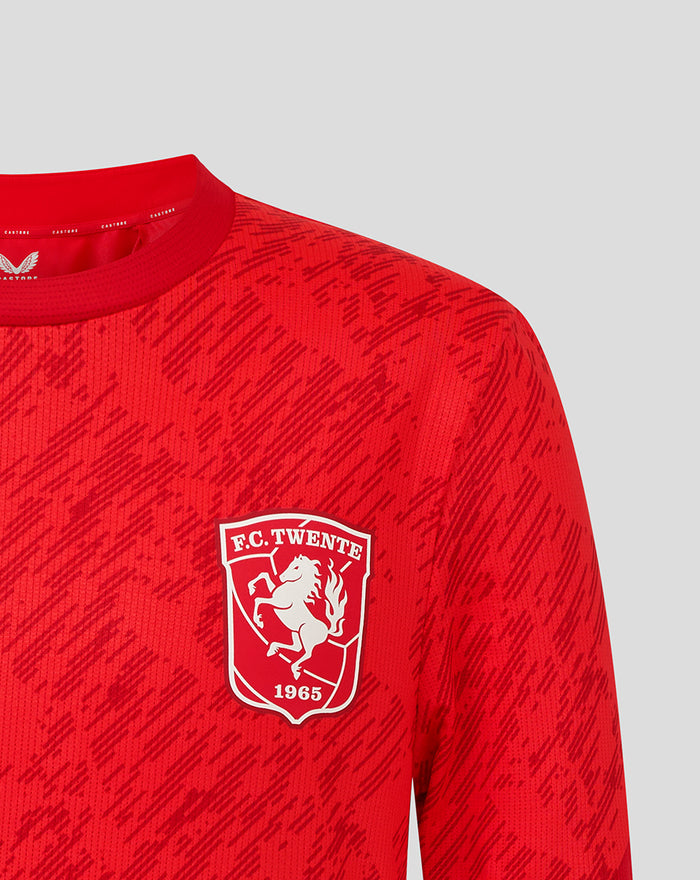Close-up of red FC Twente matchday T-shirt featuring a white crest on the chest and a printed pattern.