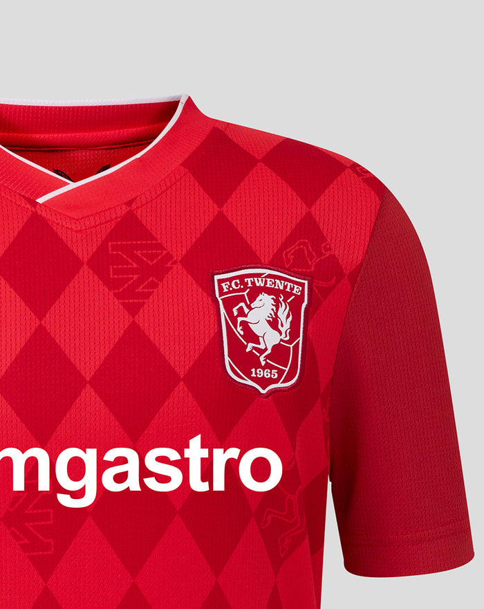 Close up of chest area on FC Twente home shirt 25/26 junior displaying the crest and ggmastro sponsor