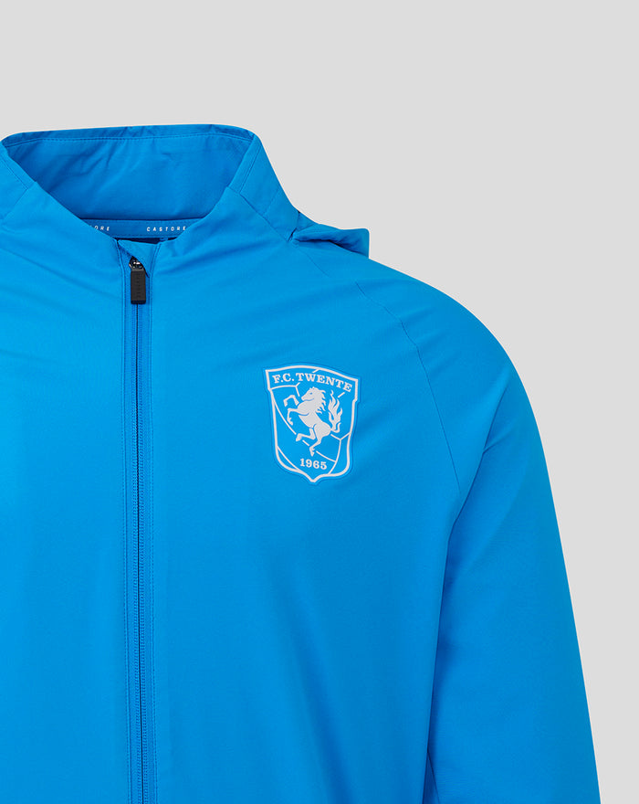 Close up of bright blue FC Twente men's rain jacket showing a white crest on the chest and a front zipper