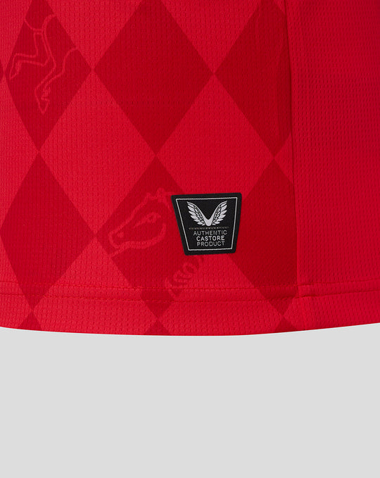 Close-up of red FC Twente home shirt fabric with a diamond pattern and authentic Castore product badge at the hem