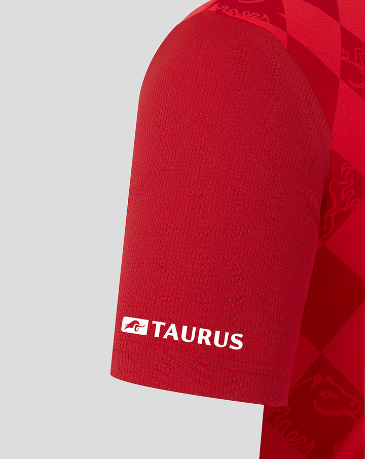 Close-up of red Twente home shirt sleeve featuring the Taurus branding in white