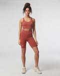 Model wearing rosewood Active Core Sports Bra with matching high-waisted shorts and small white logo on the bra.