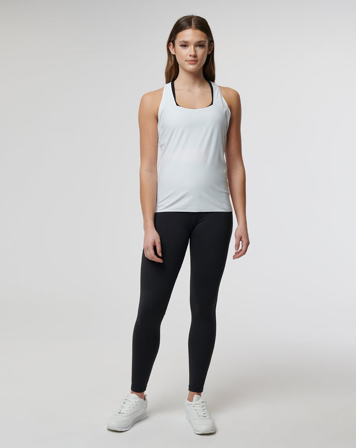 Female model wearing white lightweight Active Technical Vest with square neckline over black leggings and white sneakers.