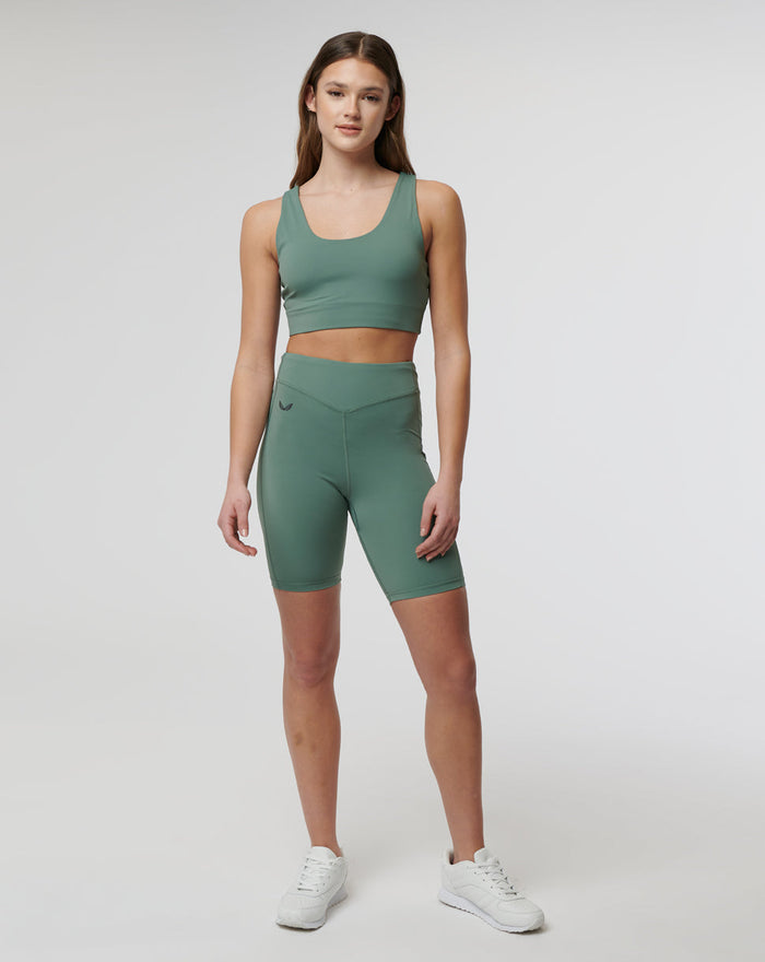 Full body shot of a model in sage green Active Elite Shorts and matching sports bra, posing in a studio with white sneakers.