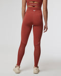 Back view of rust Rosewood Active Air Leggings on a model showing a high waistband and a white logo at the center back.