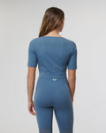 Back view of a blue cropped top with matching leggings, showing back ventilation holes and a white emblem on the waistband.