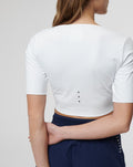 Back view of white cropped top with ventilation holes along the back and a small neck patch
